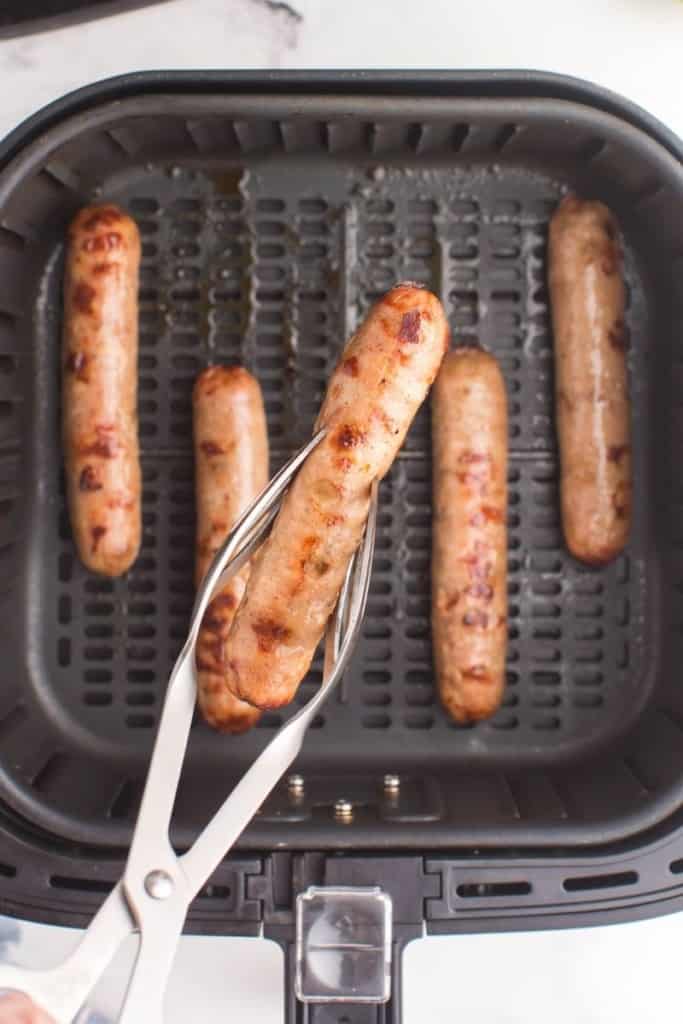 tongs lifting cooked chicken sausages out of air fryer