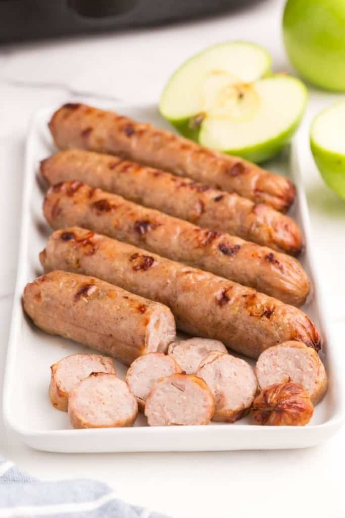 Several air fryer chicken sausages on plate with one cut into slices