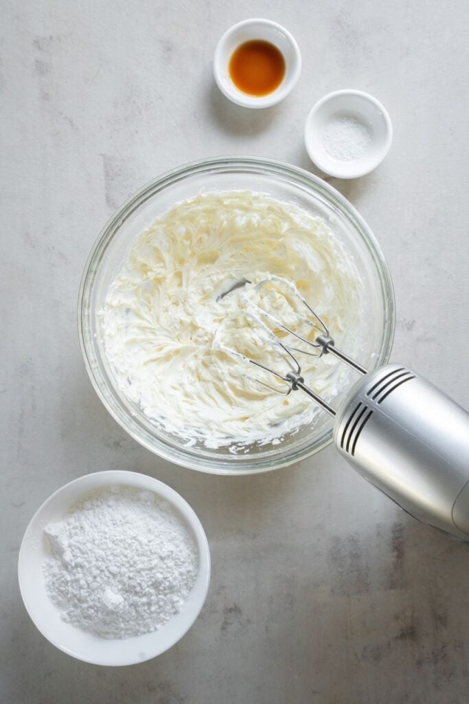 Frosting without butter being mixed with a hand mixer in a bowl.