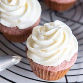 Cream cheese frosting piped on top of strawberry cupcakes.