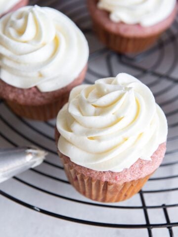 Cream cheese frosting piped on top of strawberry cupcakes.