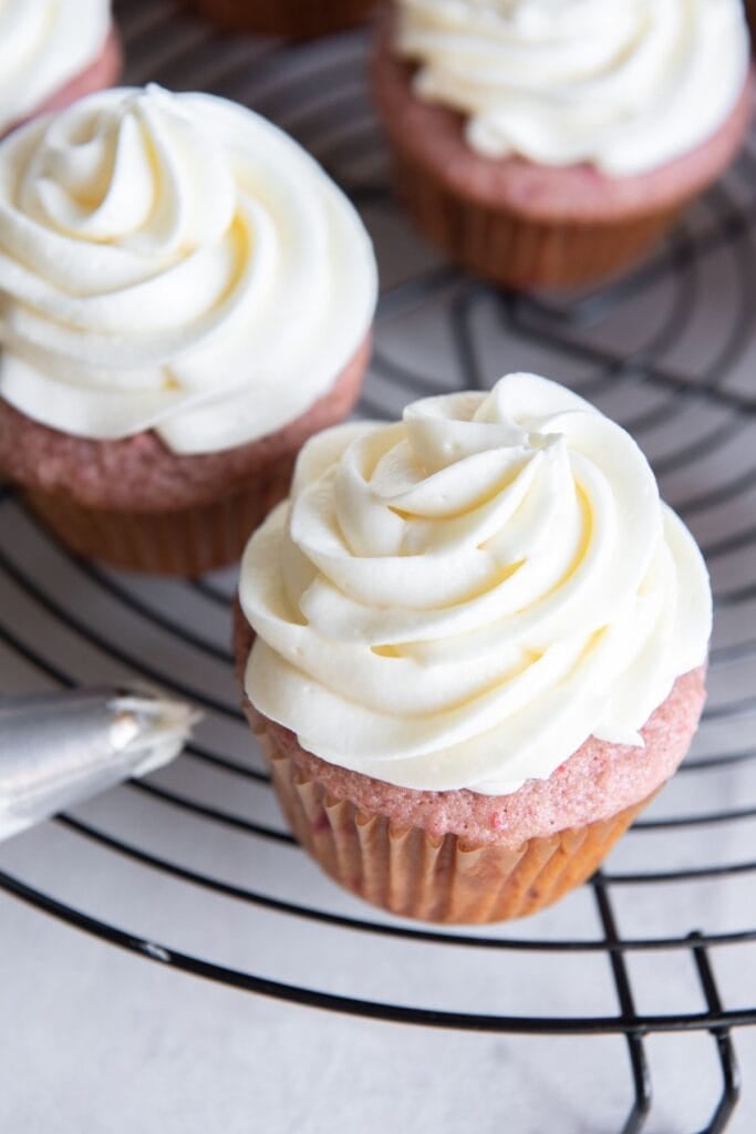 Cream cheese frosting piped on top of strawberry cupcakes.