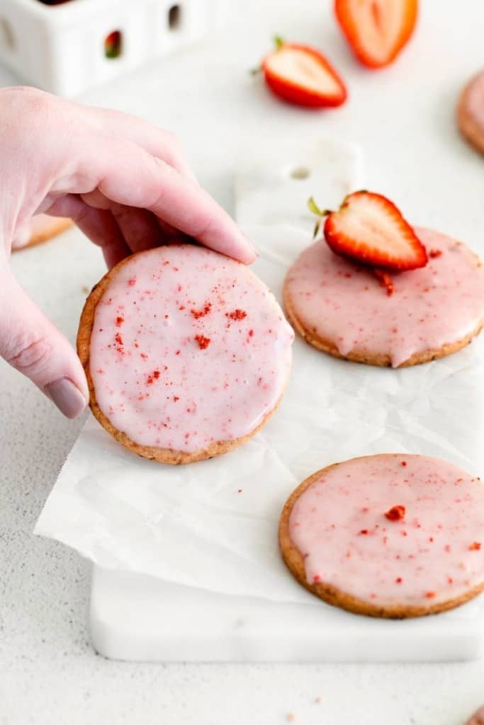 hand picking up strawberry shortbread cookie from parchment paper