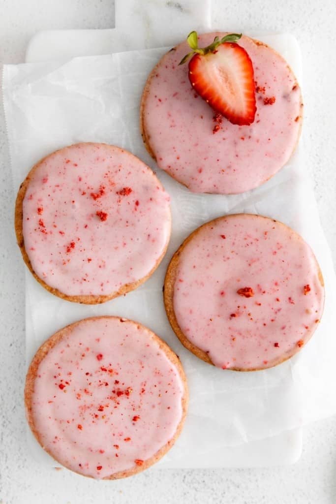 four fresh strawberry shortbread cookies with glaze on parchment paper