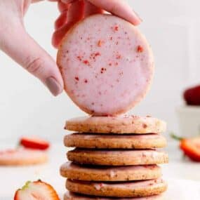 Stack of strawberry shortbread cookies with a hand displaying the top cookie