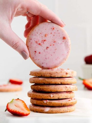 Stack of strawberry shortbread cookies with a hand displaying the top cookie