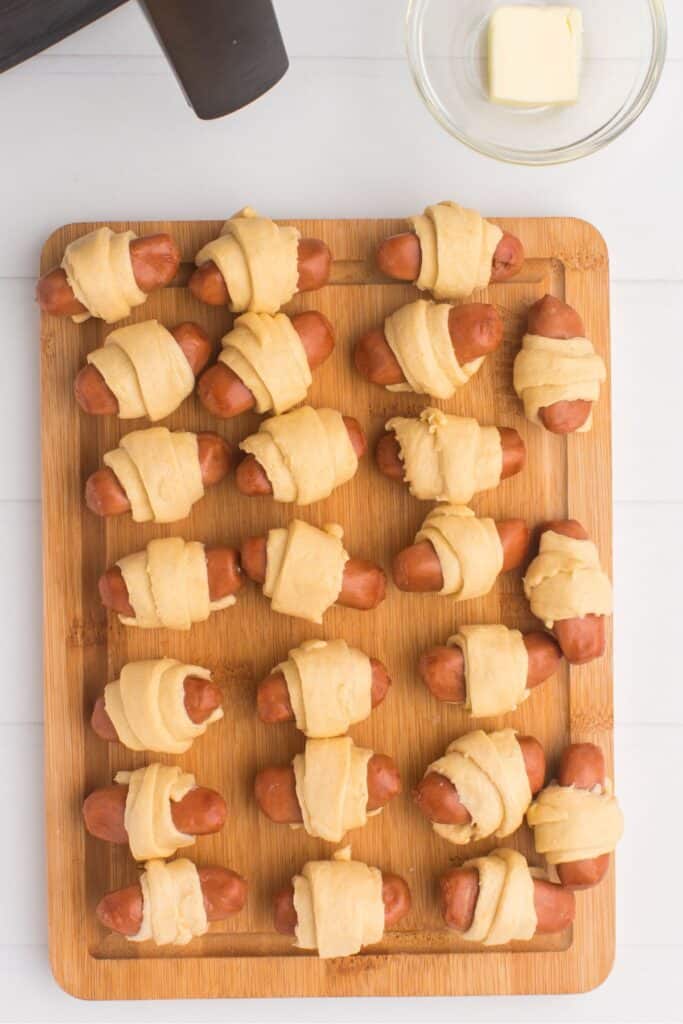 Pigs in a blanket on a cutting board and ready to be cooked.