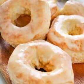 Air fryer donuts covered in glaze on a wooden serving board.