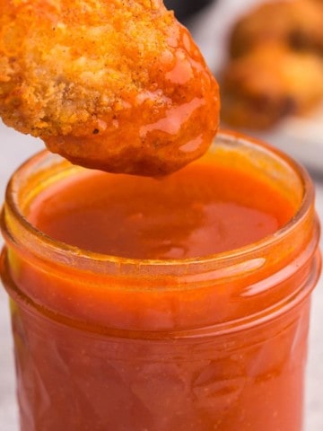 honey buffalo sauce in jar with chicken being dipped in it