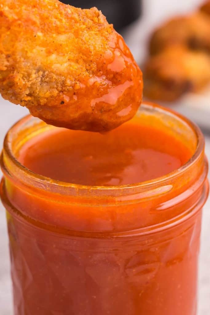 honey buffalo sauce in jar with chicken being dipped in it