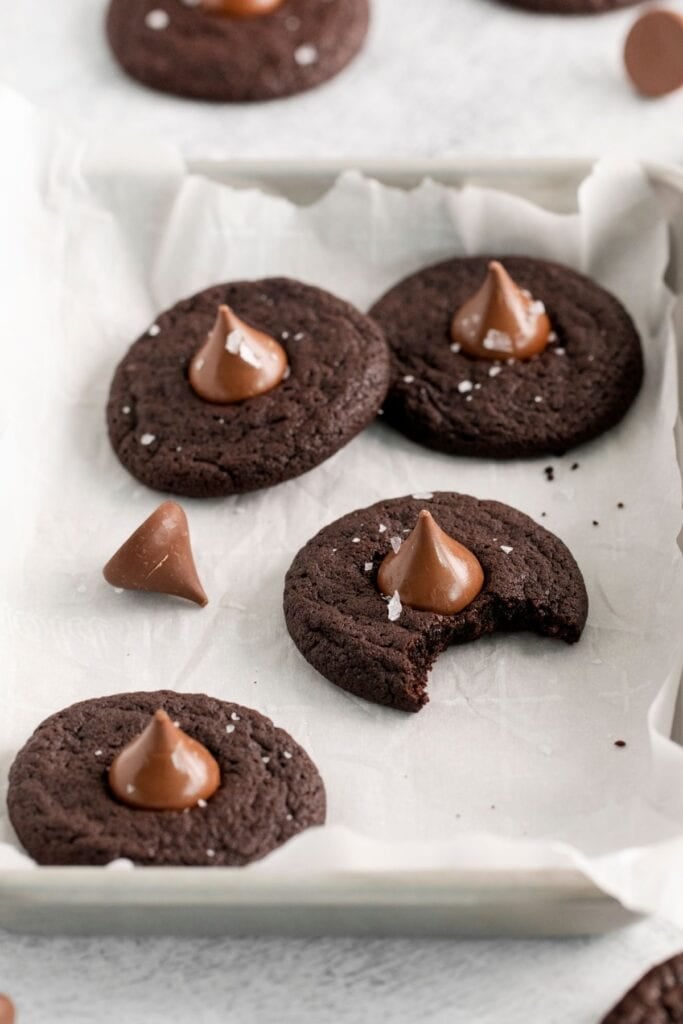 Chocolate cookie blossoms on parchment paper with one of them with a bit taken out of it.