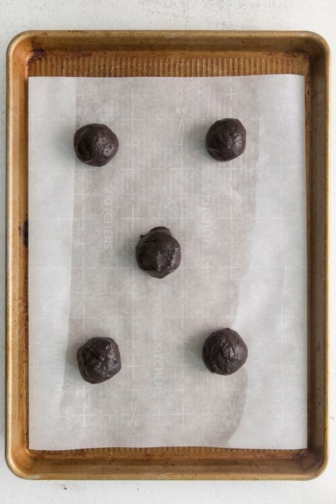 Chocolate blossoms cookies dough balls on parchment paper on a baking sheet about to be baked.