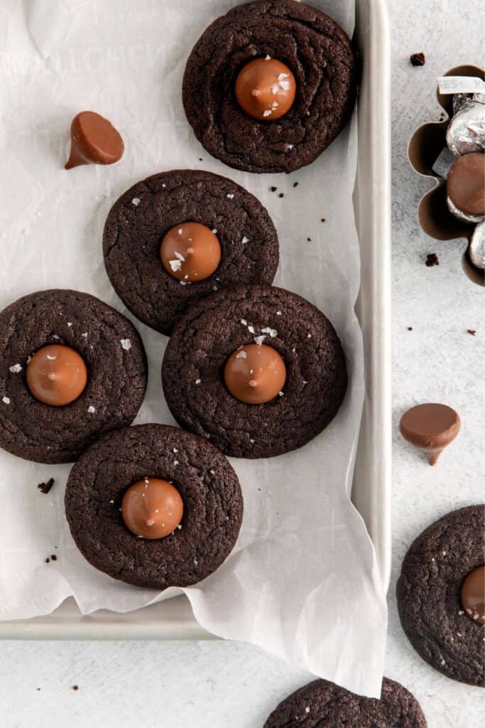 Chocolate Christmas cookies with Hershey kisses on top on parchment paper in a storage dish.