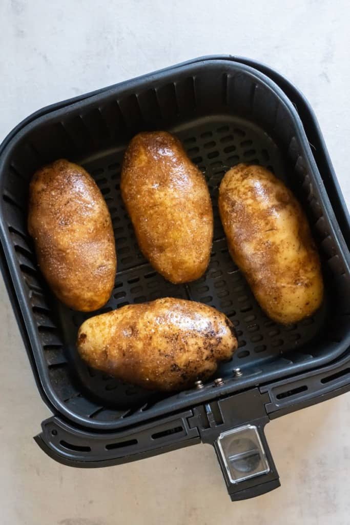 four raw baked potatoes in an air fryer basket