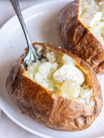 air fryer baked potatoes on a plate with a fork in one of them
