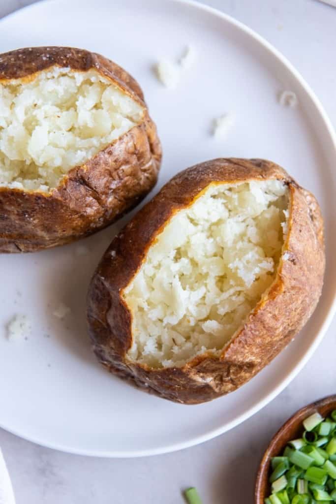 two freshly air fried baked potatoes on a white plate.