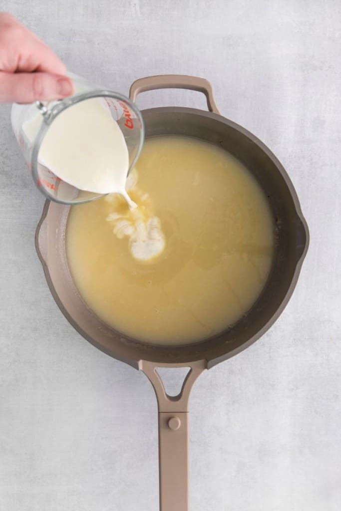 pouring heavy cream into the sauce for a green bean casserole