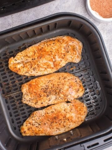 Cooked grilled chicken in an air fryer basket.
