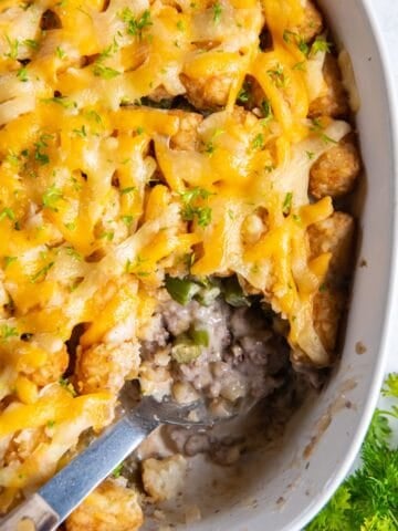 Overhead view of tater tot casserole with green beans with a serving spoon inside and a scoop missing.