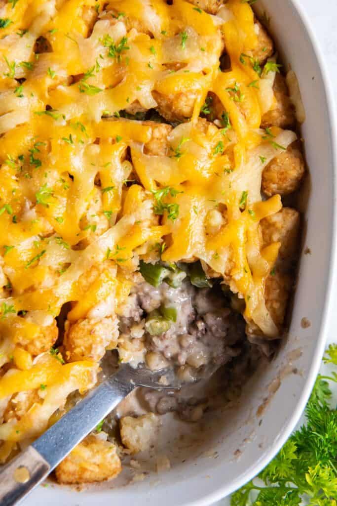 Overhead view of tater tot casserole with green beans with a serving spoon inside and a scoop missing.