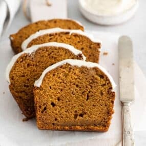 Pumpkin bread with cream cheese sliced and placed on a plate with a knife next to it.