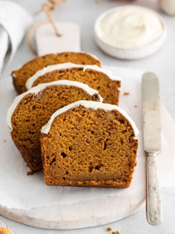 Pumpkin bread with cream cheese sliced and placed on a plate with a knife next to it.