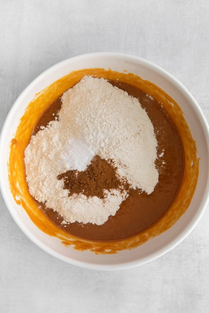 Dry ingredients added into the white mixing bowl (flour, pumpkin spice, and baking soda).
