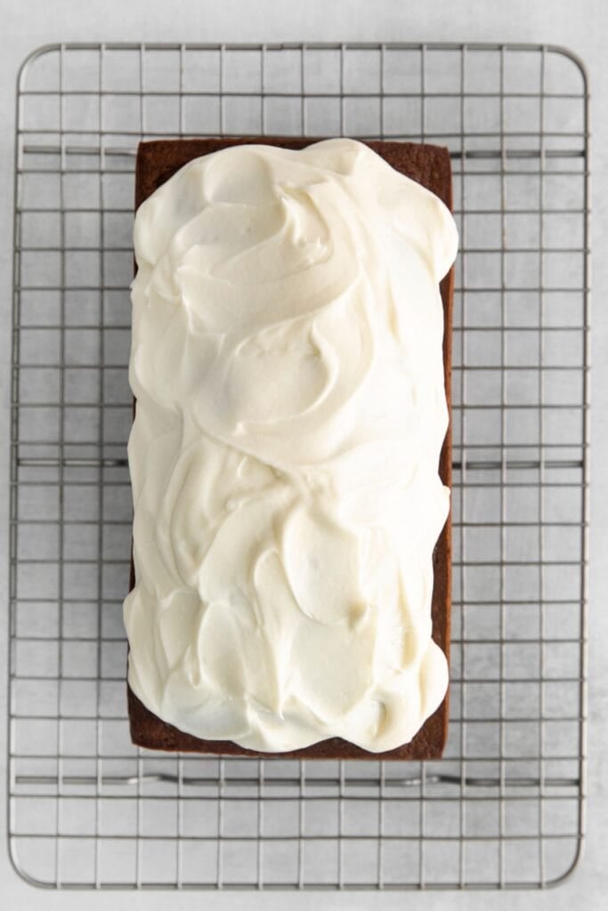 Pumpkin bread with cream cheese frosting being spread on top on a cooling wire rack.
