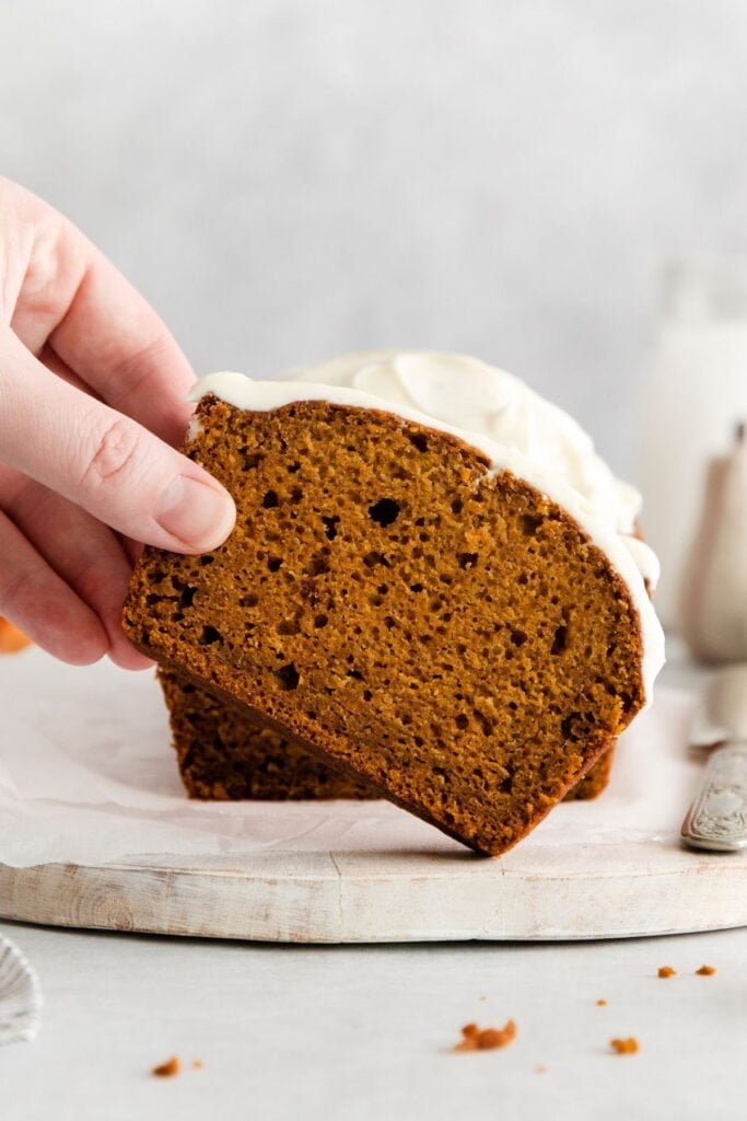A slice of pumpkin bread with cream cheese being picked up.
