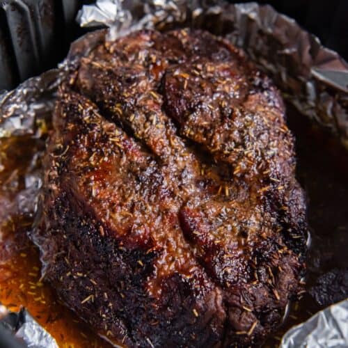 Cooked chuck roast in an air fryer basket with foil and juices around it.