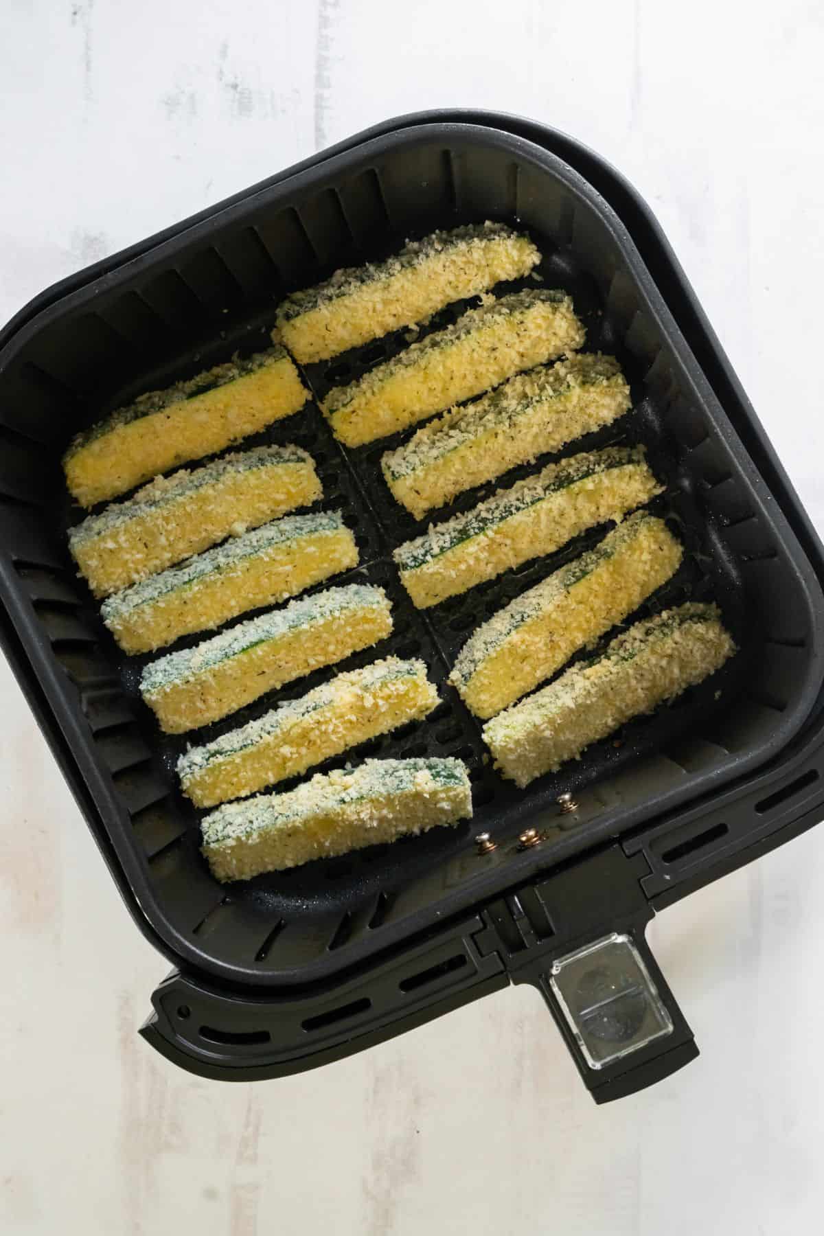 Zucchini fries in an air fryer basket ready to be cooked.