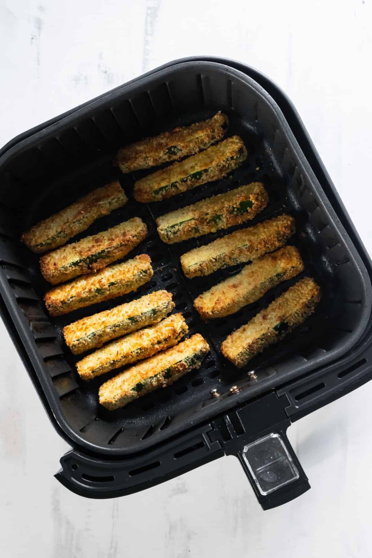 Golden brown zucchini fries in an air fryer basket.