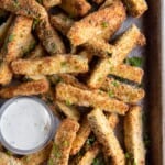 Overhead view of air fryer zucchini fries on a baking pan with a side of sauce.
