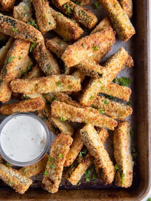 Overhead view of air fryer zucchini fries on a baking pan with a side of sauce.