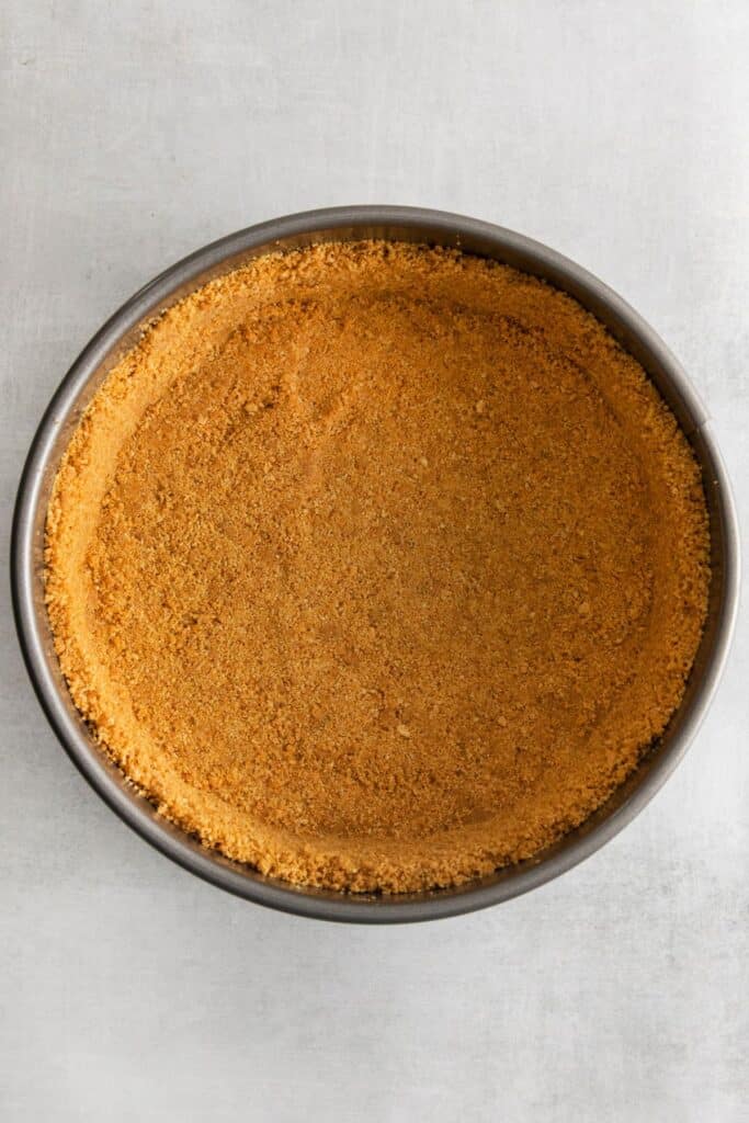Graham cracker crust pressed into springform pan to make apple caramel cheesecake.