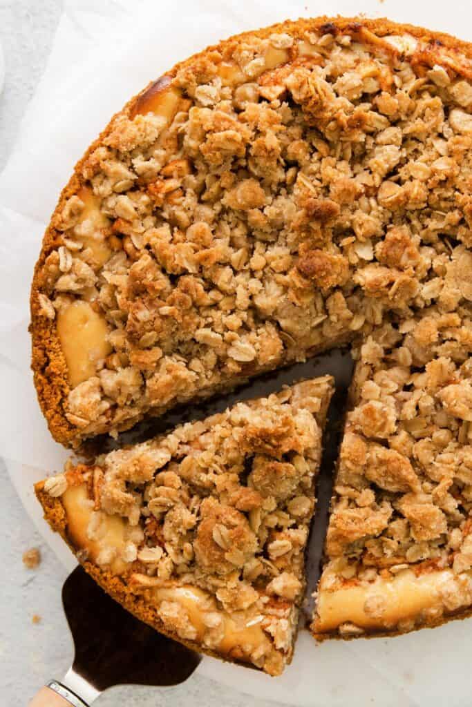 Fully baked caramel apple cheesecake recipe with a slice cut out about to be picked up by cake spatula.