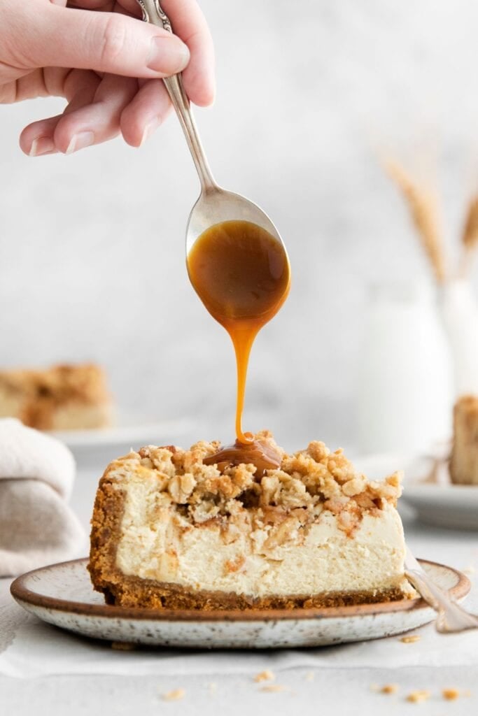 Extra caramel sauce being drizzled on top of a slice of apple cheesecake.