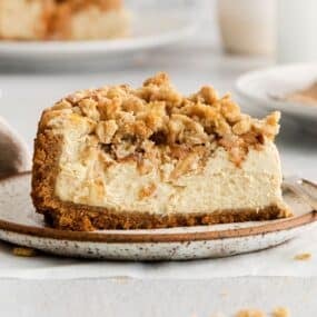 A close up of the apple crumble cheesecake so you can see the crust, caramel cheesecake, apple topping, then sweet crumble topping.