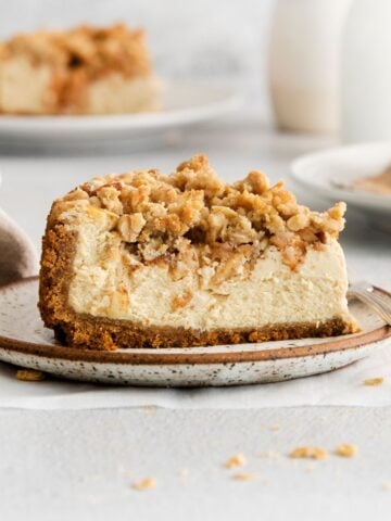 A close up of the apple crumble cheesecake so you can see the crust, caramel cheesecake, apple topping, then sweet crumble topping.