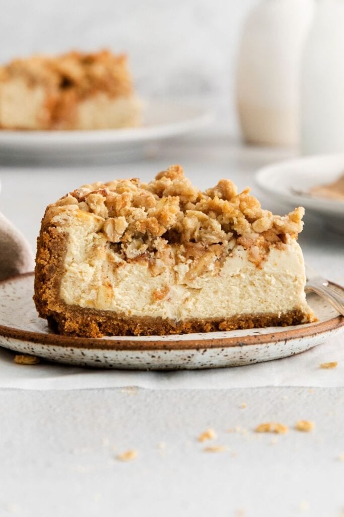 A close up of the apple crumble cheesecake so you can see the crust, caramel cheesecake, apple topping, then sweet crumble topping.