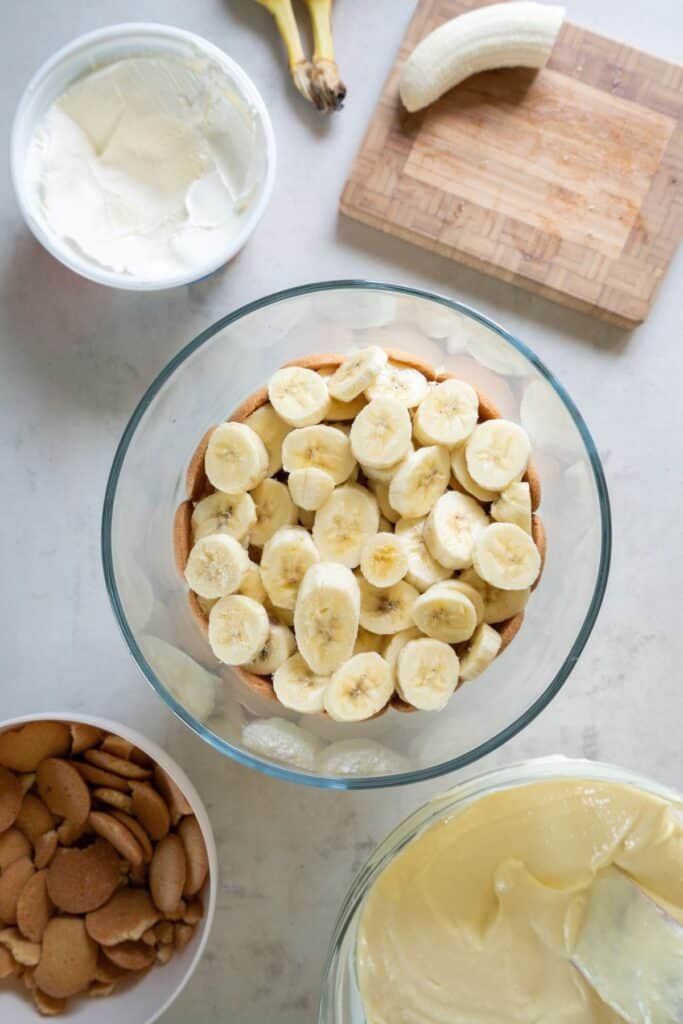 Bananas being layered on top of Nilla wafer to make banana pudding with cool whip.