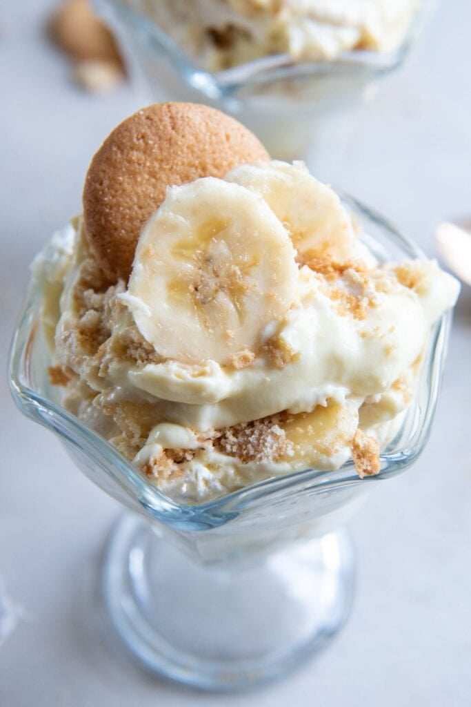 Close up banana pudding with sour cream in a small individual serving bowl with banana slices and a Nilla wafer on top.