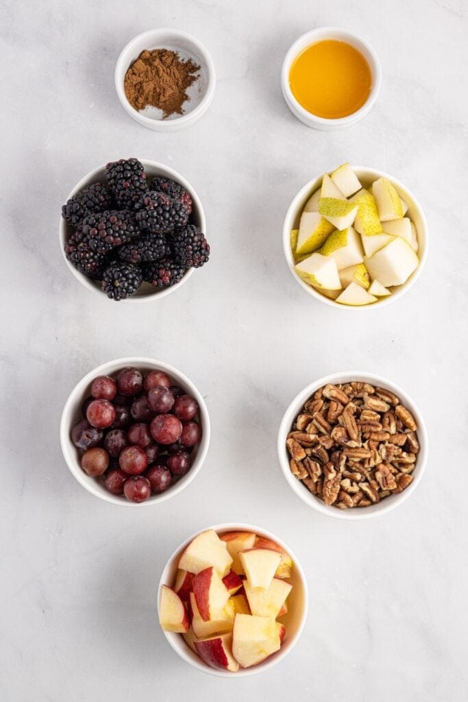 Ingredients needed to make fall fruit salad: apple, pear, cinnamon, orange juice, grapes, blackberries, and pecans.