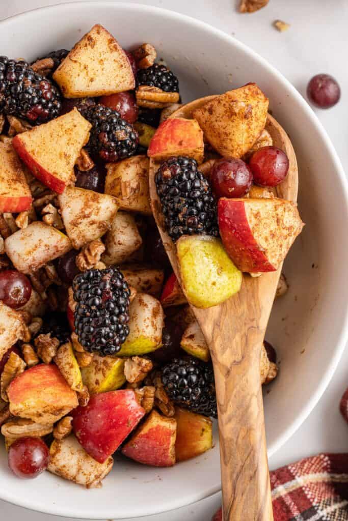Close up of fall fruit salad in a white bowl with a wooden spoon.