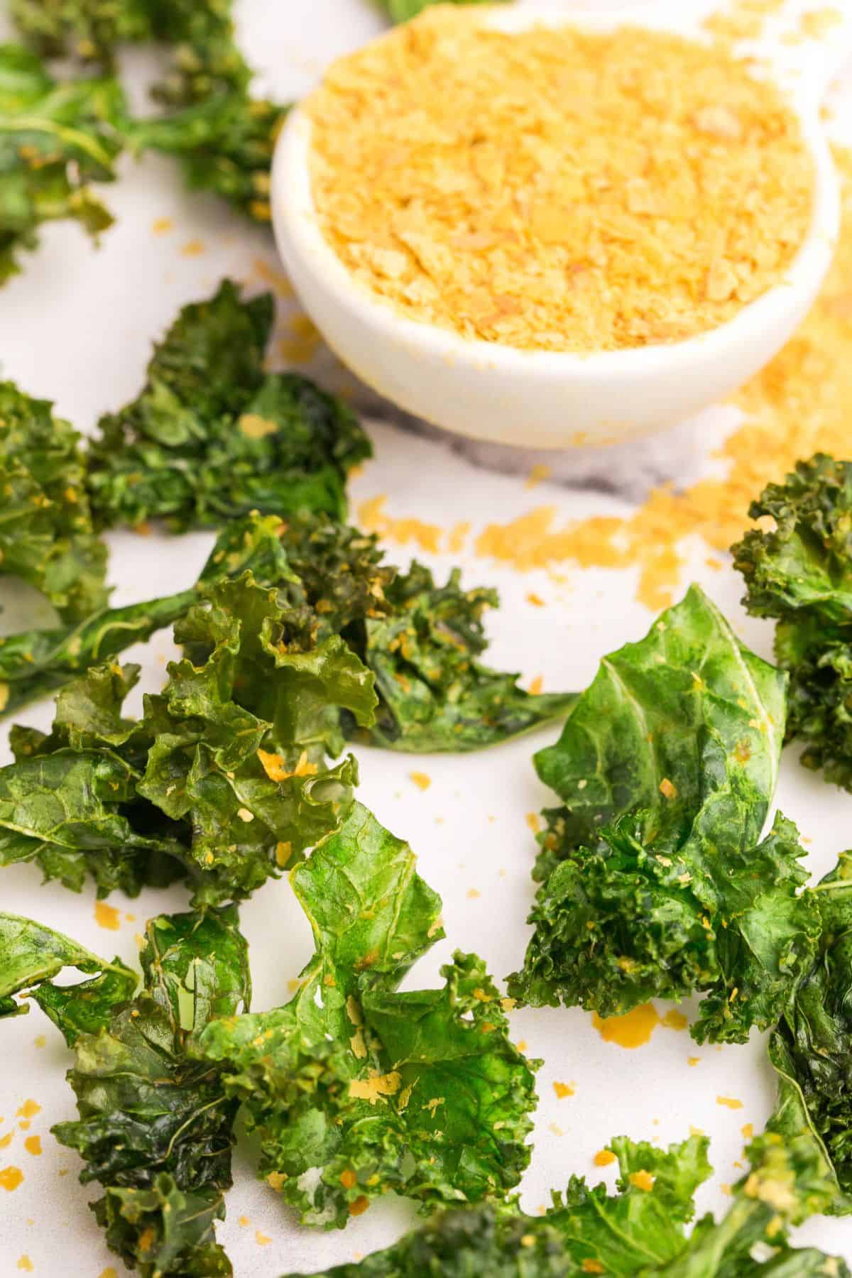 Air fried kale chips on a white serving tray with some more nutritional yeast on the side.