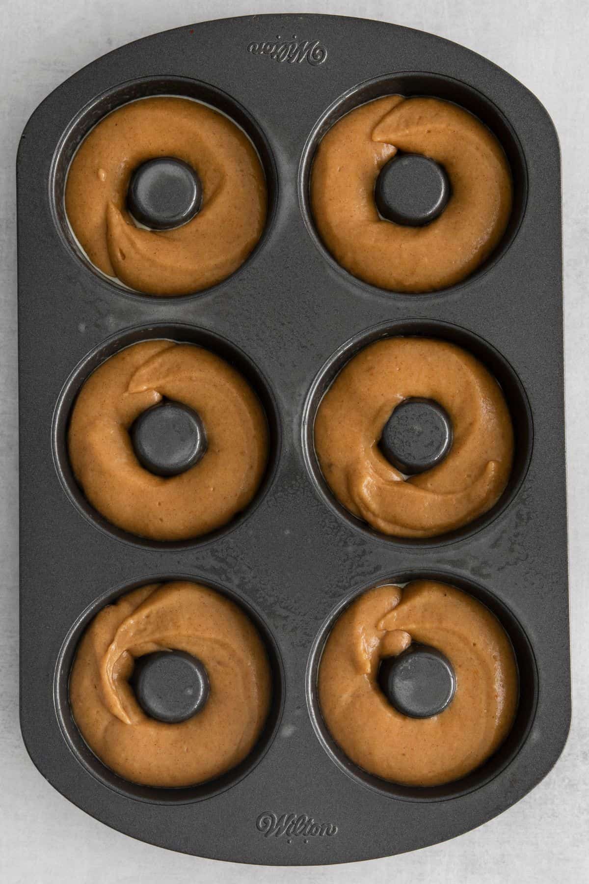 Pumpkin spice donuts piped into the donut pan.