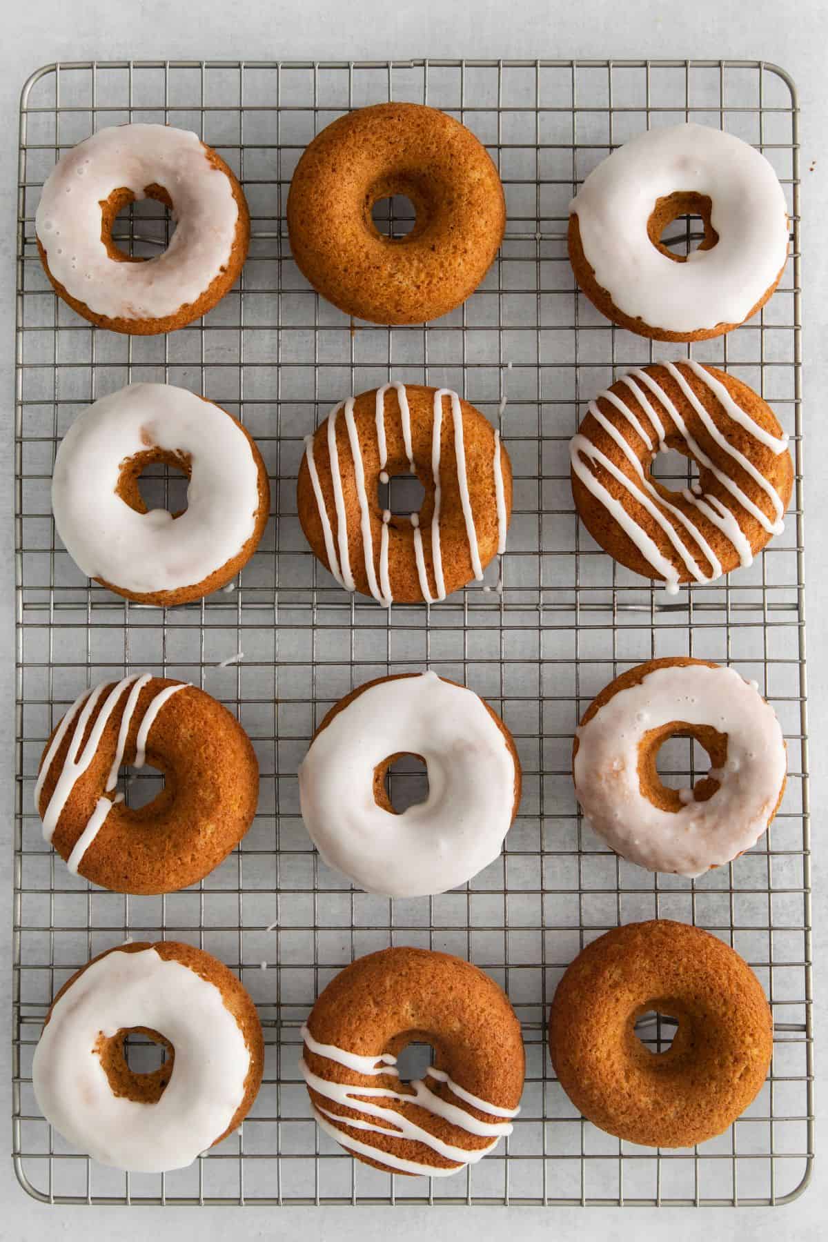 Baked pumpkin spice donuts on a wire rack with icing on top of them. Some fully covered on top and some with lines of icing on them.