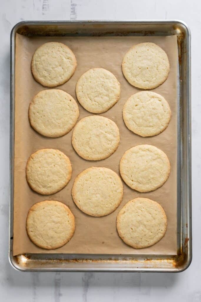 Baked homemade sugar cookies on a baking sheet on parchment paper.