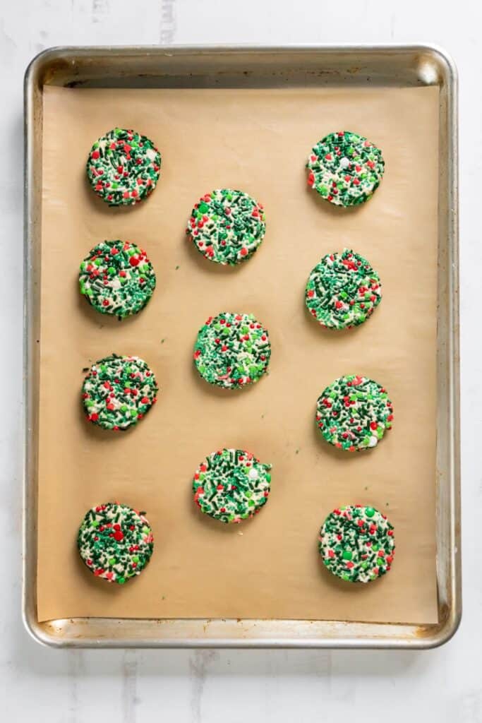 Easy sugar cookie recipe on a baking sheet with parchment paper with Christmas sprinkles on them.