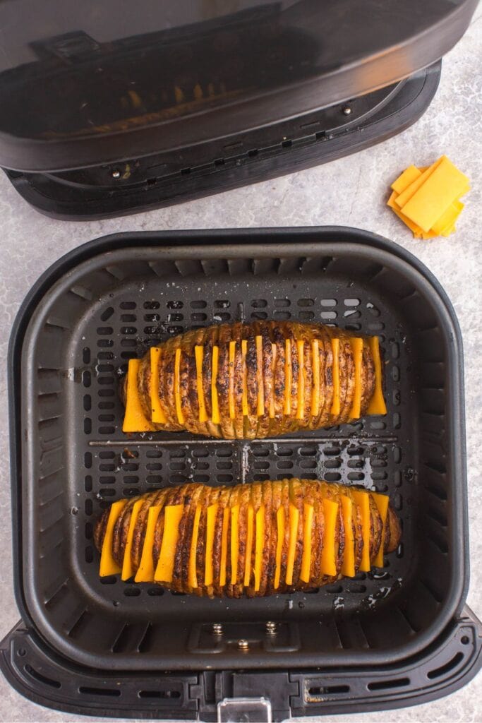 Cooked hasselback potatoes in the air fryer with cheddar cheese slices being added in between each cut slice.
